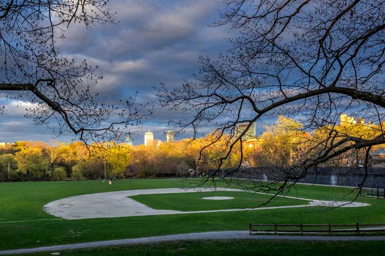 Dusk falls on a little league field in Brookline Massachusetts with the towers of Boston in the background